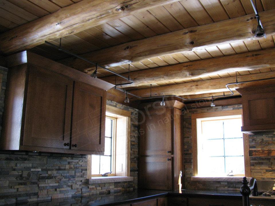 Norstone Ochre Blend Rock Panels on a Rustic Kitchen Backsplash featuring prominent exposed natural log beams on the ceiling